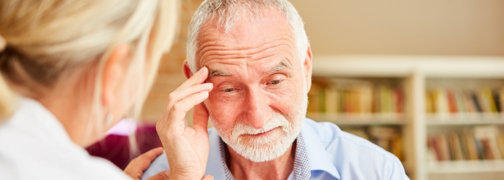 An older man touching his head in confusion while a doctor comforts him.