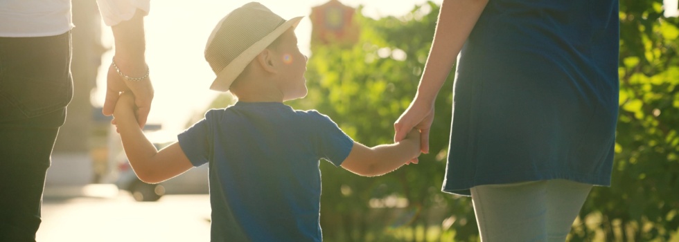 A family with a young child holding hands outdoors.