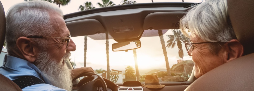 A happy older couple driving in a convertible car.