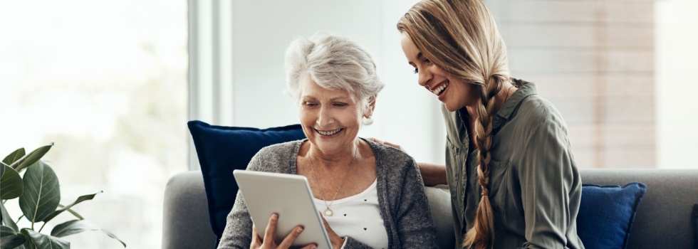 A woman showing her adult daughter something on a tablet.