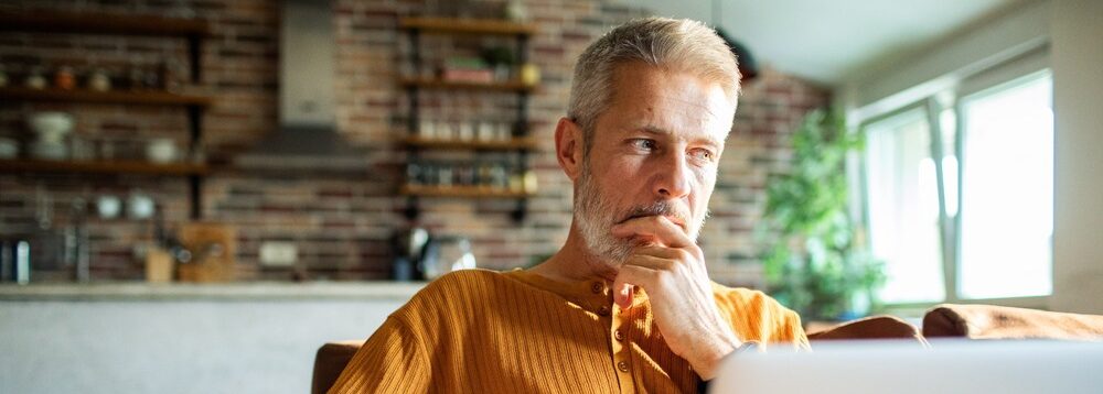 A man in his 50s thinking while using a laptop