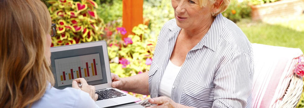 Female financial planner showing a senior woman charts on a laptop.