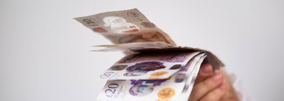 A hand holding UK bank notes.