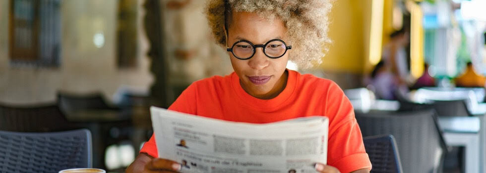 A woman reading a newspaper in a café.
